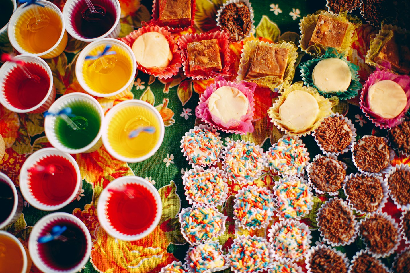 Assorted Brazilian sweets and gelatin cups arranged on a floral tablecloth.