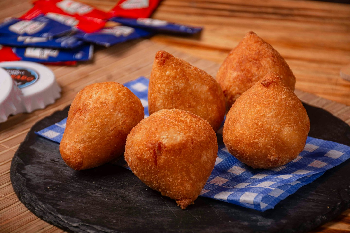 Five golden-brown crispy coxinhas sit on a dark slate board.