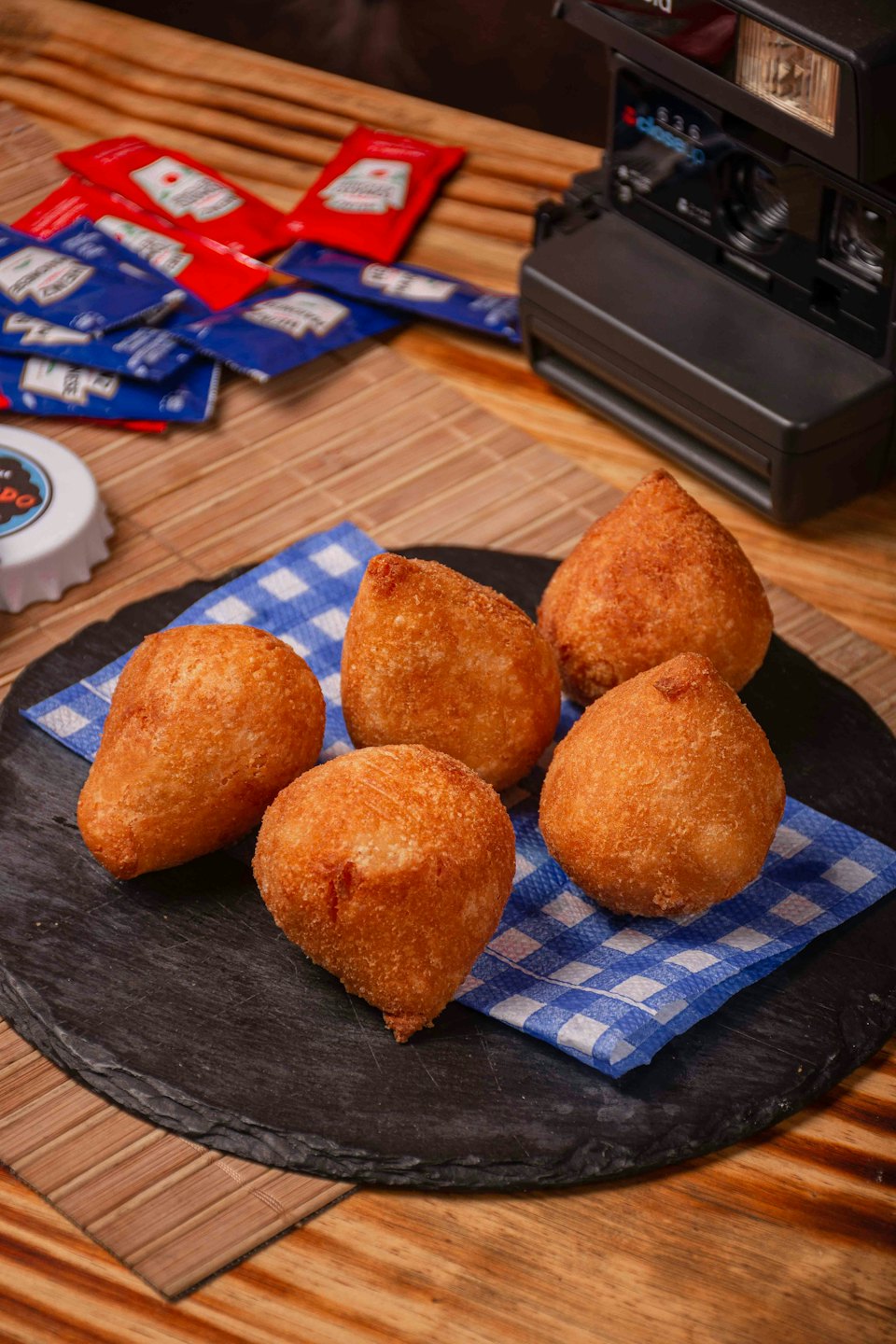 Five golden fried coxinha snacks on a black slate platter.
